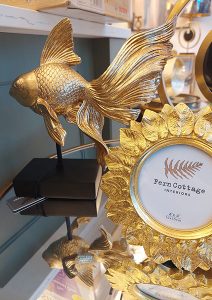 golden metal goldfish on console table beside a golden picture frame 